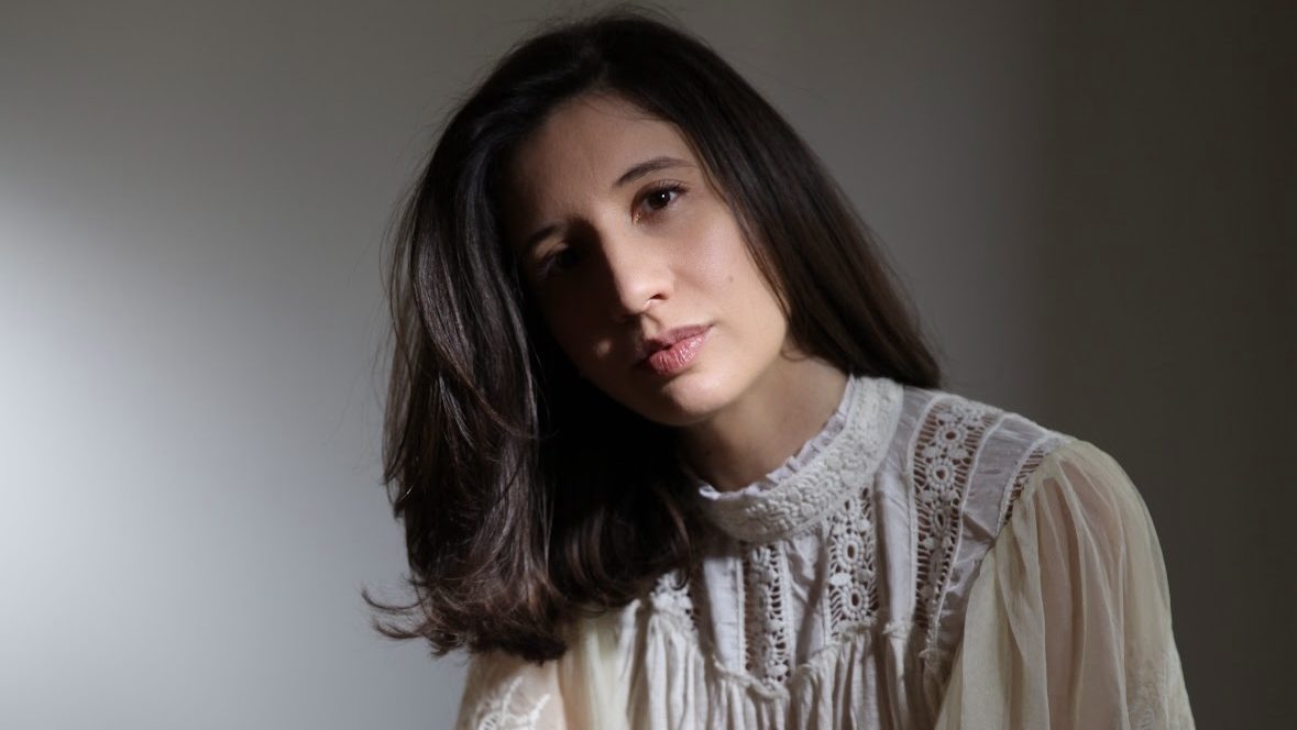 woman with long brown hair and white blouse looking towards the camera