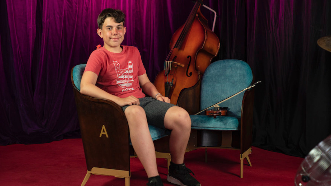 Arturs sitting on a chair looking at the camera, with a double bass behind him