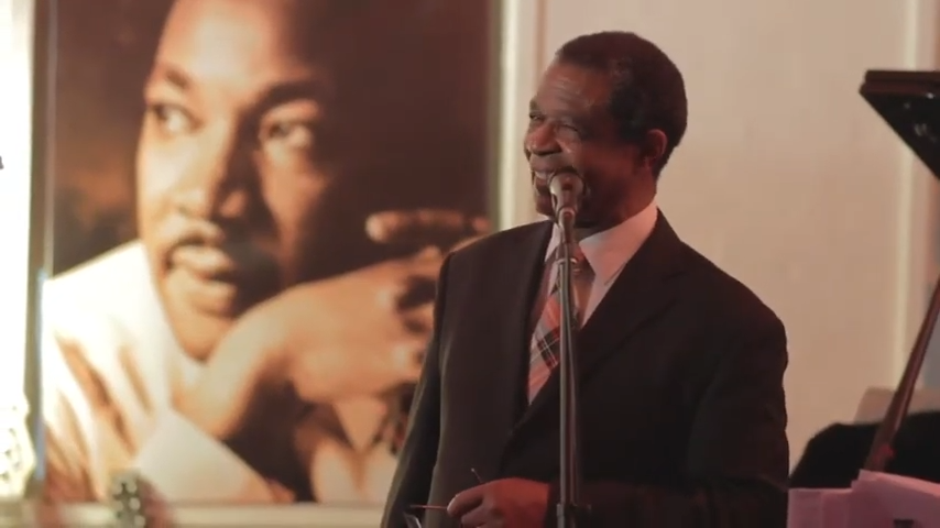 Man speaking with Martin Luther King photo in background
