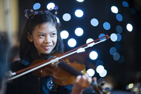 A young girl plays violin, sparkling lights behind