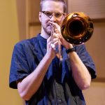 Trombonist wearing a dark blue shirt, looks directly to camera