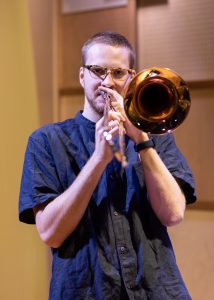 Trombonist wearing a dark blue shirt, looks directly to camera