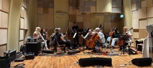 An ensemble of a dozen musicians, casually dressed, in a recording session