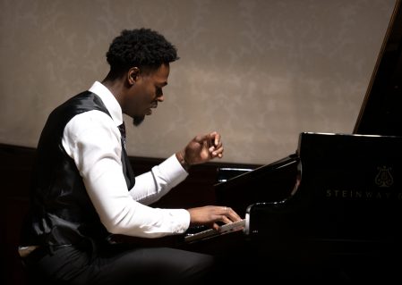 Pianist Josiah Wade, in formal white shirt and waistcoat playing a Steinway Grand